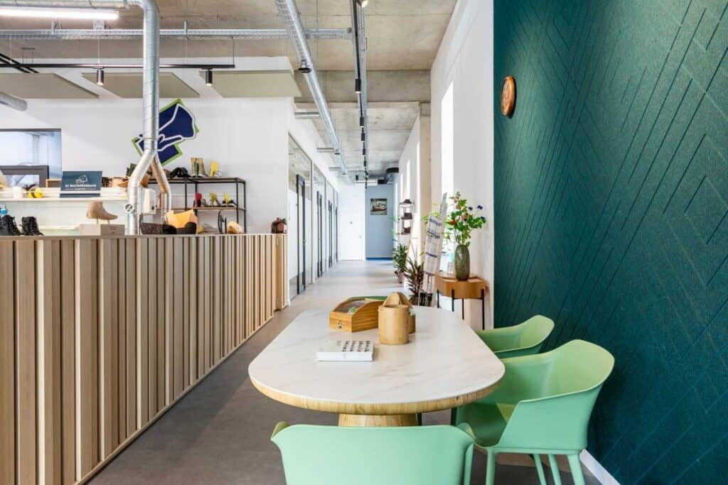 Impressie van een werkplaats voor maatschoenen. De werkplaats heeft een wandpaneel van akoestisch PET-vilt, een bedrijfslogo van akoestisch PET-vilt en akoestische plafondeilanden.