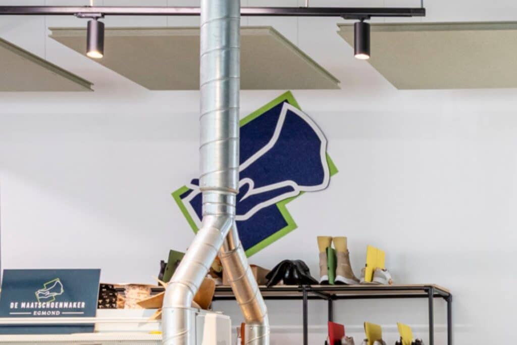 Impressie van een werkplaats met op de wand een bedrijfslogo, gemaakt van drie lagen akoestisch PET-vilt: blauw, groen en wit.