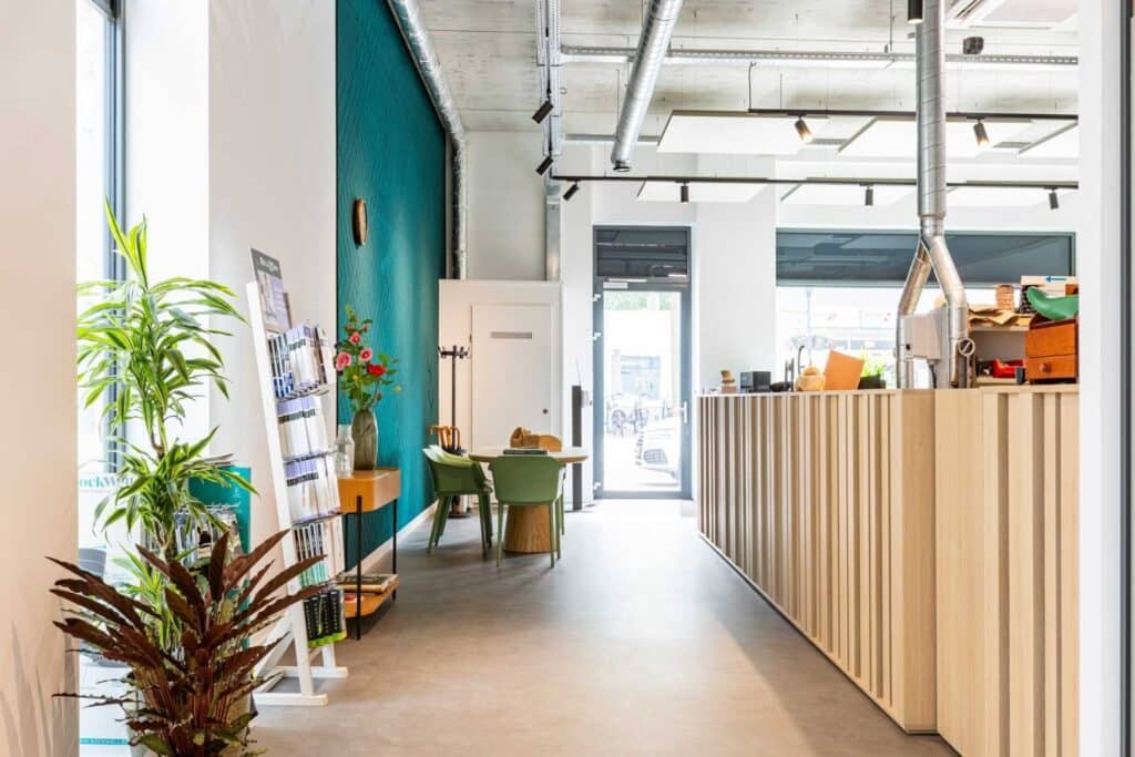 Impressie van een werkplaats voor maatschoenen. De werkplaats heeft een diepgroen wandpaneel van akoestisch PET-vilt en akoestische plafondeilanden in grijs.