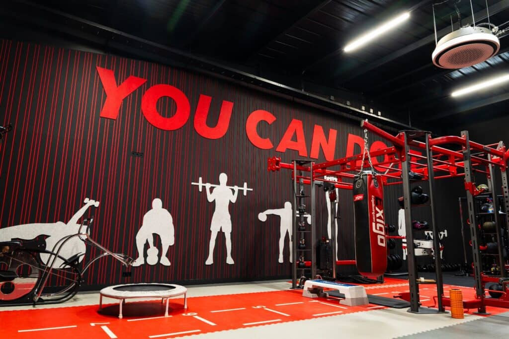 Impressie van een fitnessruimte in een bedrijf, voorzien van lattenwanden van akoestisch PET-vilt in rood en antraciet.
