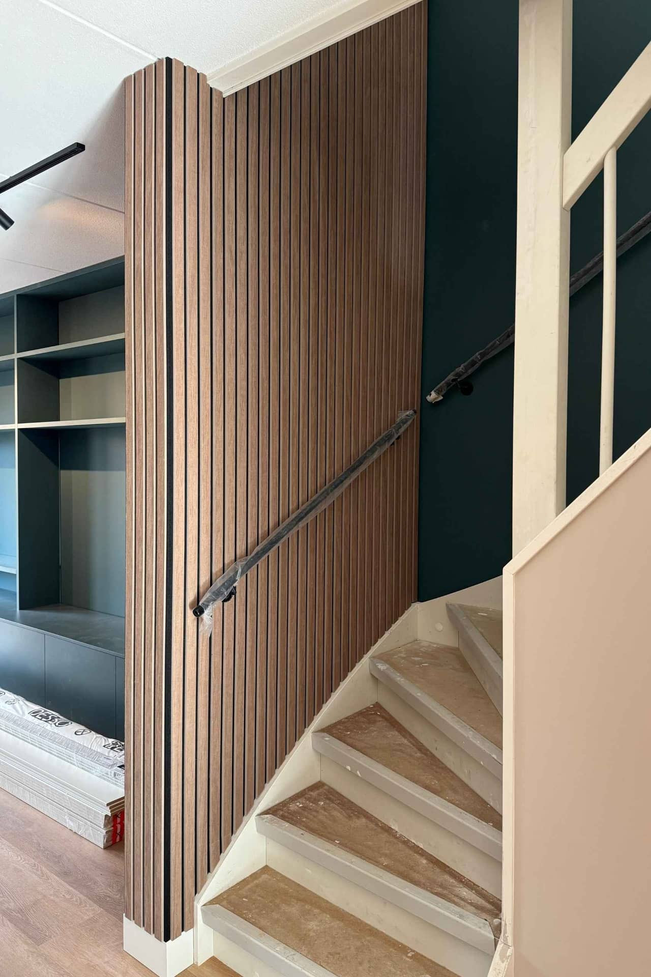 Impressie van een woonkamer die wordt ingericht, onder meer met een trapwand van akoestische houtlook panelen, gemaakt van PET-vilt van Tacito.